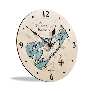 Puede incluir: Un reloj de madera con un mapa de las Mil Islas en la esfera. El reloj tiene agujas negras y una rosa de los vientos en la esquina inferior derecha. El reloj est&aacute; hecho por Sea & Soul.