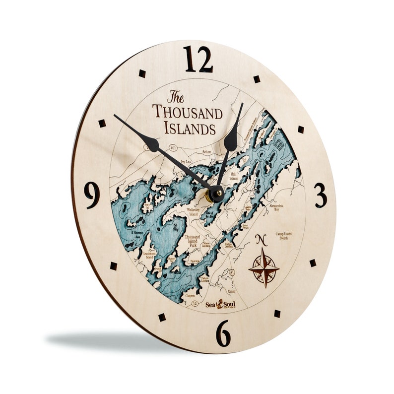 Puede incluir: Un reloj de madera con un mapa de las Mil Islas en la esfera. El reloj tiene agujas negras y una rosa de los vientos en la esquina inferior derecha. El reloj est&aacute; hecho por Sea & Soul.