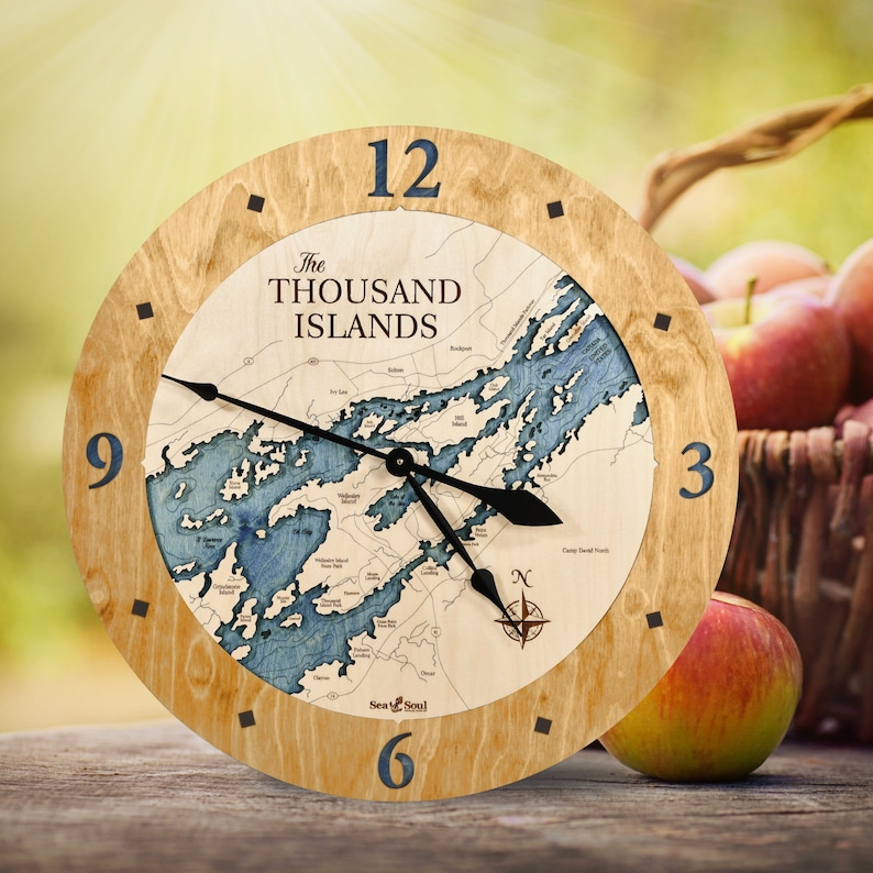 Puede incluir: Un reloj de madera con un mapa de las Mil Islas en la esfera. El reloj tiene un marco de madera clara y agujas negras. El mapa es azul y blanco y muestra las islas del r&iacute;o San Lorenzo.