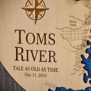 May include: A wooden sign with a map of Toms River, New Jersey. The sign is engraved with the words "Toms River", "Tale as old as time", and "May 11, 2019".