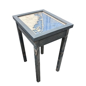 Puede incluir: Una mesa auxiliar de madera con un acabado teñido gris. La parte superior presenta un mapa enmarcado de Long Beach Island, Nueva Jersey, con un diseño náutico azul y blanco.