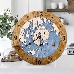 May include: A wooden clock with a nautical map of Bar Harbor, Maine. The clock face features a compass rose and the words "Bar Harbor, Maine". The clock is surrounded by a brown wooden frame.