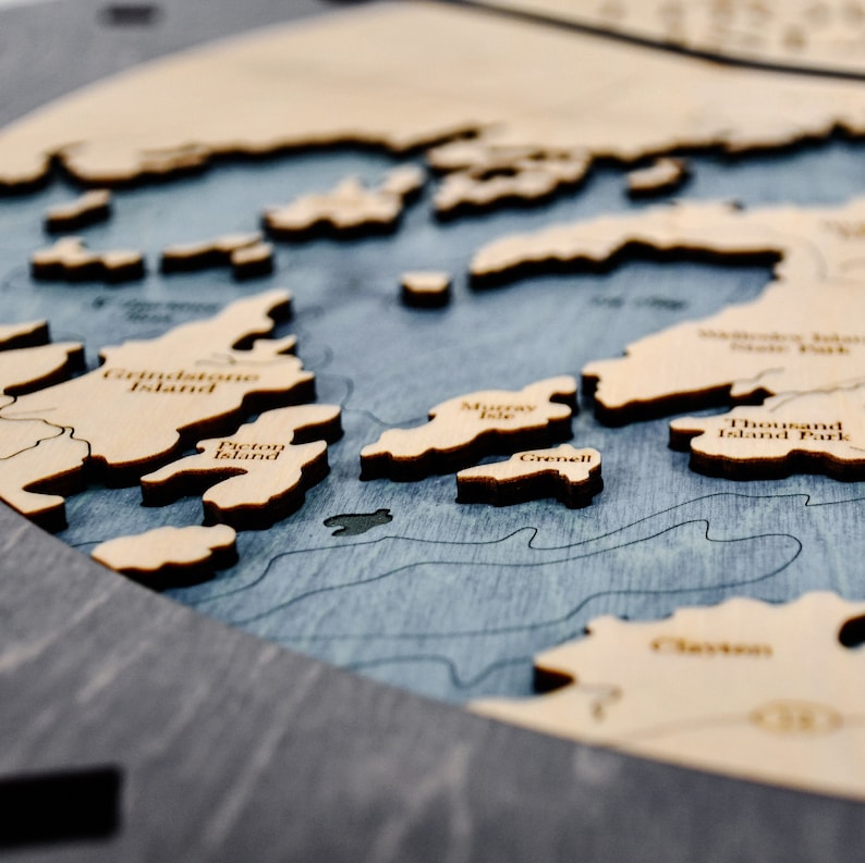 Puede incluir: Primer plano de un mapa de madera de una masa de agua con islas. Las islas est&aacute;n etiquetadas con nombres como "Grindstone Island", "Picton Island", "Murray Isle", "Grenell" y "Thousand Island Park".