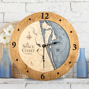May include: A wooden clock with a map of the Space Coast of Florida. The clock face is brown with black numbers and hands. The map is blue and white and shows the coastline of the Space Coast. The clock is 12 inches in diameter.