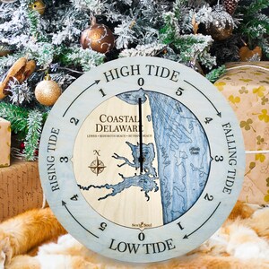 May include: A wooden tide clock with a blue and white map of Coastal Delaware. The clock face shows the tide levels, with "High Tide" at the top and "Low Tide" at the bottom. The clock is surrounded by a light blue ring with the words "Rising Tide" and "Falling Tide" marked on it.