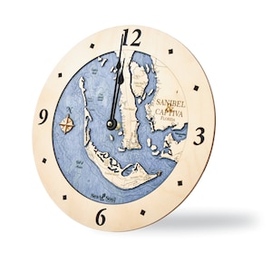 May include: A wooden clock with a blue and white map of Sanibel and Captiva Islands, Florida. The clock face has black hands and black Roman numeral hour markers. The clock is labeled "Sea & Soul!" at the bottom.