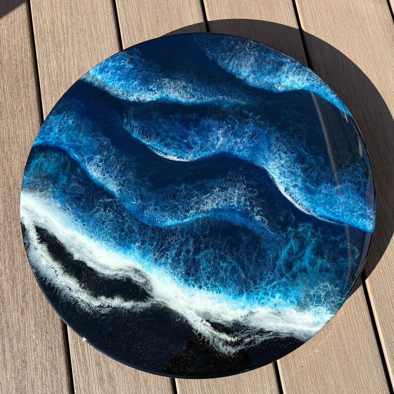 May include: A round resin art piece with a blue and white abstract design resembling ocean waves. The background is black.
