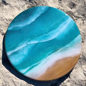 May include: Round wooden serving tray with a blue and white resin ocean wave design. The tray has a light brown wood border.