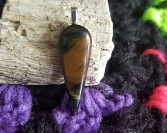 May include: A teardrop-shaped pendant made of tiger's eye gemstone with a silver bail. The stone has a brown and gold color with a chatoyant effect.