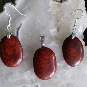 May include: A set of red jasper earrings and pendant with silver hooks and bail. The stones are oval shaped and have a mottled red and brown pattern.