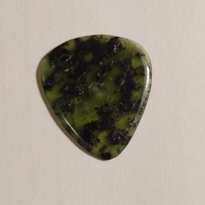 Puede incluir: Una púa de guitarra verde y negra hecha de piedra. La púa tiene un patrón veteado único.