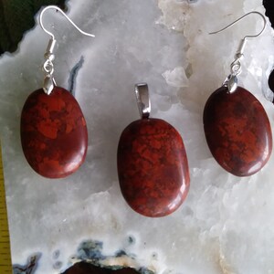 May include: A set of red jasper earrings and a pendant with silver-toned findings. The stones are oval shaped and have a mottled red and brown pattern.