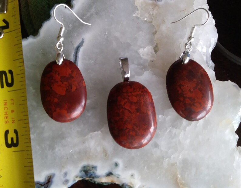 May include: A set of red jasper earrings and a pendant with silver-toned findings. The stones are oval shaped and have a mottled red and brown pattern.