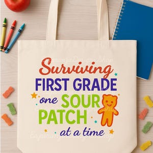 May include: Cream-colored tote bag with the text "Surviving First Grade one SOUR PATCH at a time." The bag has a colorful design with a gummy bear illustration. An apple, crayons, and a blue notebook are also visible.