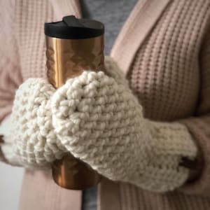 May include: A pair of white crocheted hand warmers with a copper travel mug inside. The hand warmers are made with a chunky yarn and have a simple stitch pattern.