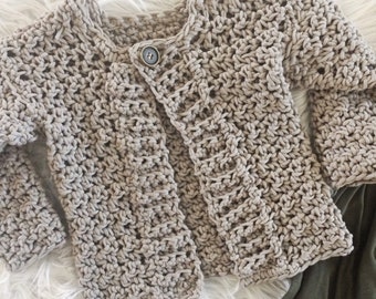May include: A beige crocheted cardigan with a button closure. The cardigan is made with a textured stitch and has a relaxed fit.