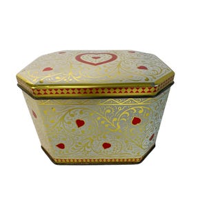 Puede incluir: Una caja de lata octogonal con fondo blanco, adornada con filigranas doradas y detalles de corazones rojos. La tapa presenta un gran corazón en el centro. Los bordes están adornados con un patrón geométrico rojo y dorado. Un recipiente decorativo.