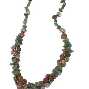 May include: A necklace featuring a mix of light green stone chips, small round gold-toned beads, and spiral-shaped tan and pink seashells. The strand is arranged with clusters of these elements and secured with a metal toggle clasp at the top.
