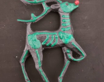 Puede incluir: Un adorno de reno negro y verde con un diseño de esqueleto. El reno tiene la nariz roja y las astas verdes.