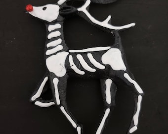 Puede incluir: Un adorno de reno esquelético en blanco y negro con la nariz roja. El reno está de pie sobre sus patas traseras con las patas delanteras levantadas.