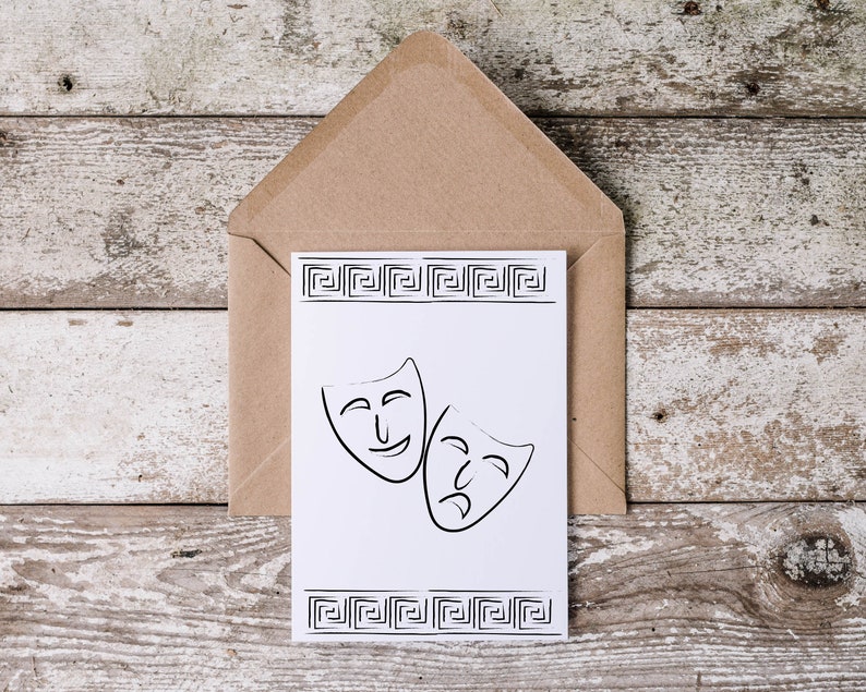 May include: A white card with a black and white illustration of two theater masks. The masks are a happy face and a sad face. The card is in a brown envelope. The card has a Greek key border.
