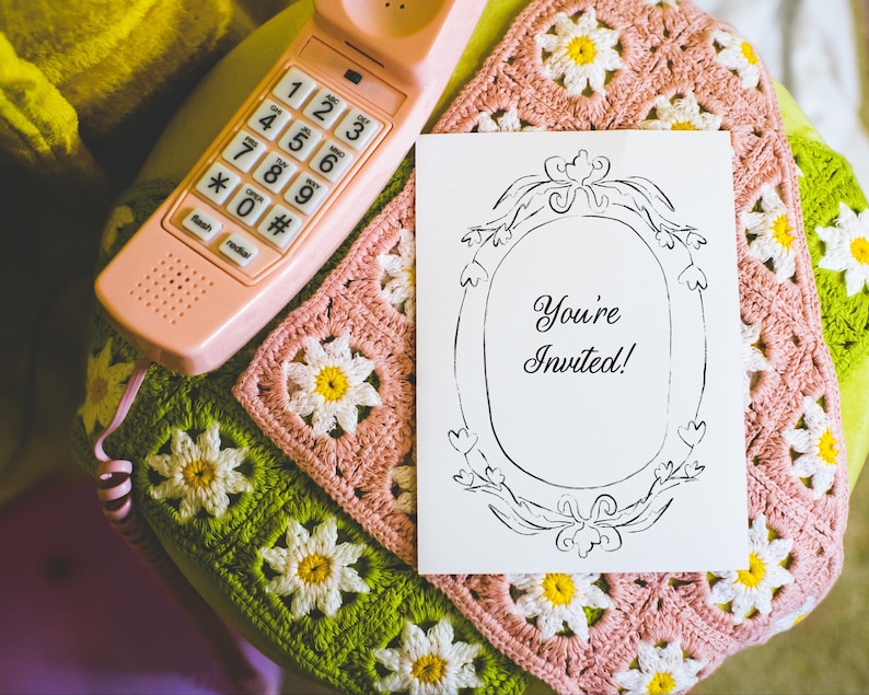 May include: A vintage-style scene featuring a pink rotary phone and a greeting card that says "You're Invited!" The card is set on a handmade crochet blanket with daisy patterns in pink, green, and yellow. The phone is a retro design.