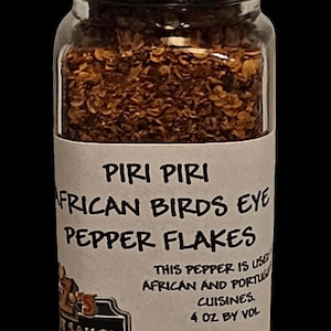 May include: A clear glass jar filled with red pepper flakes, topped with a black lid. The label reads "PIRI PIRI AFRICAN BIRDS EYE PEPPER FLAKES." The jar contains 4 oz by volume of pepper flakes. The label also mentions the pepper is used in African and Portuguese cuisines.