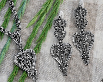 May include: A silver necklace and earrings set with a heart-shaped pendant and matching earrings. The jewelry features intricate filigree designs.