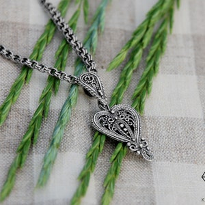 May include: A silver necklace with a detailed heart-shaped pendant. The pendant has a filigree design and is hanging on a chain.