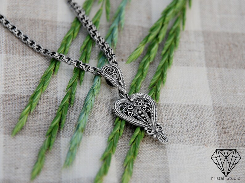 May include: A silver necklace with a detailed heart-shaped pendant. The pendant has a filigree design and is hanging on a chain.