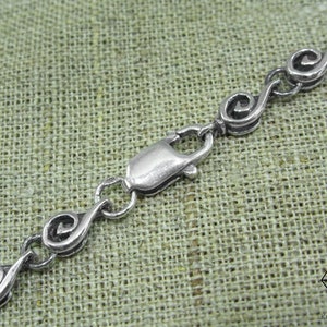 May include: A silver chain necklace with a clasp closure. The chain is made of small, linked, spiral-shaped pieces.