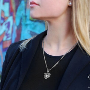May include: A silver chain necklace with a detailed silver heart pendant. The pendant has a small clear stone in the center.