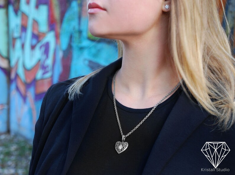 May include: A silver chain necklace with a detailed silver heart pendant. The pendant has a small clear stone in the center.