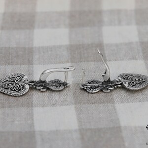 May include: A pair of silver filigree earrings with a heart-shaped design. The earrings are dangle style and have a hook closure.