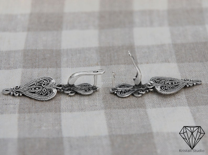 May include: A pair of silver filigree earrings with a heart-shaped design. The earrings are dangle style and have a hook closure.