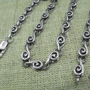 May include: A silver chain necklace with a unique spiral link design. The chain is made of polished silver and has a lobster claw clasp.
