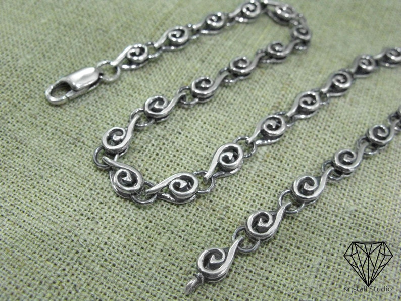 May include: A silver chain necklace with a unique spiral link design. The chain is made of small, interconnected spirals that create a flowing, elegant look.