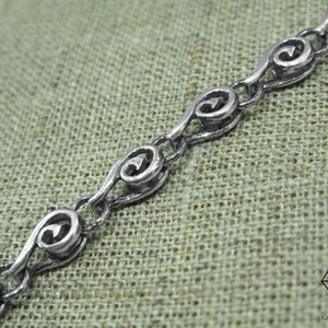 May include: A silver chain necklace with a repeating pattern of stylized hearts. The chain is made of small, interconnected links.