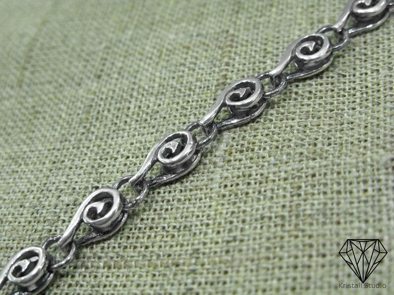 May include: A silver chain necklace with a repeating pattern of stylized hearts. The chain is made of small, interconnected links.
