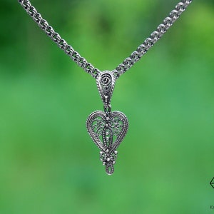 May include: A silver chain necklace with a delicate filigree heart pendant. The pendant is intricate and detailed, with a delicate design.