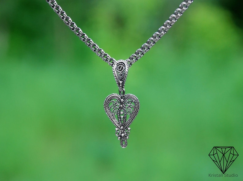 May include: A silver chain necklace with a delicate filigree heart pendant. The pendant is intricate and detailed, with a delicate design.