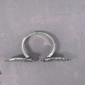 May include: A silver ring with two wings that open and close. The wings are detailed with a textured design.