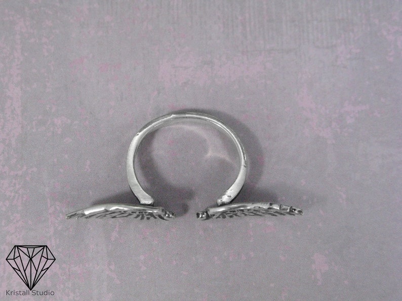 May include: A silver ring with two wings that open and close. The wings are detailed with a textured design.