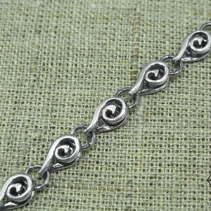 May include: A silver chain bracelet with a delicate, intricate design. Each link features a swirling pattern, creating a flowing and elegant look.