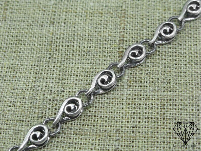 May include: A silver chain bracelet with a delicate, intricate design. Each link features a swirling pattern, creating a flowing and elegant look.