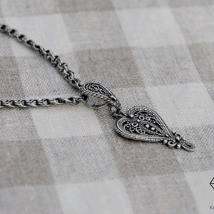 May include: A silver necklace with a detailed heart pendant. The pendant has a filigree design and is attached to a delicate chain.