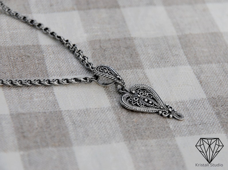 May include: A silver necklace with a detailed heart pendant. The pendant has a filigree design and is attached to a delicate chain.