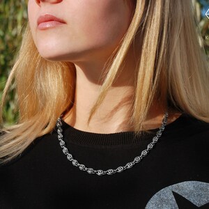 May include: A close-up of a woman wearing a black shirt with a silver chain necklace. The chain is made of small, linked circles.