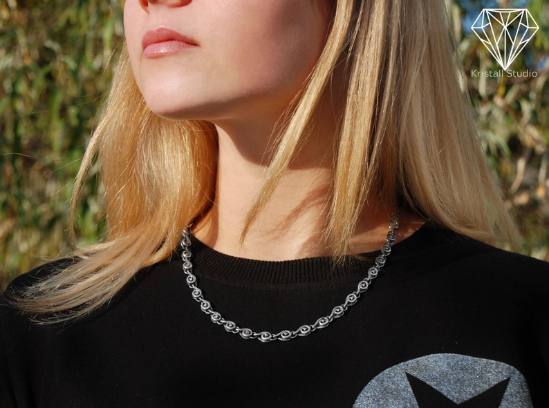 May include: A close-up of a woman wearing a black shirt with a silver chain necklace. The chain is made of small, linked circles.