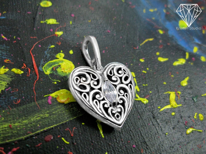 May include: A silver heart-shaped pendant with an intricate filigree design and a clear crystal in the center.